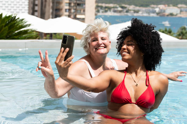 istock Two happy female friends taking a selfie in a pool during summer vacation 2202531703