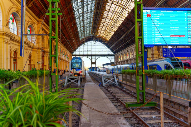 Budapest, Hungary - November 24, 2024: Interior view of the Eastern Railway Station in Budapest, featuring train tracks, digital timetable, and architectural design elements.