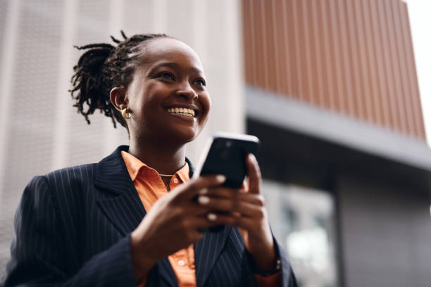 istock Smiling black businesswoman using smartphone in front of modern building 2202543066