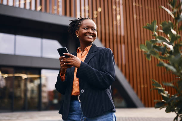 istock Smiling businesswoman using smartphone in front of modern office building 2202543231