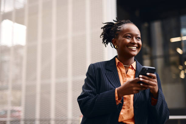istock Smiling businesswoman using smartphone in front of office building 2202543236