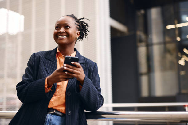 Smiling businesswoman using smartphone in urban setting, looking up
