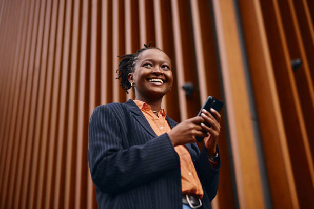 istock Smiling businesswoman using smartphone in front of modern building 2202543409