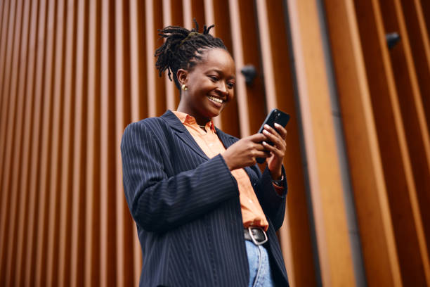 istock Smiling businesswoman using smartphone in front of modern building 2202543411