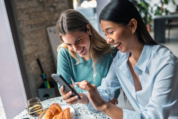 istock Two beautiful women friends talking while using smartphone in a coffee shop 2202546567