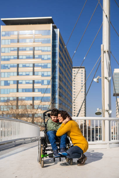 istock Mother hugging her  son with disability  in a wheelchair on a bridge 2202552834