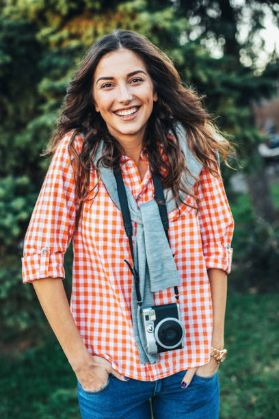Beautiful girl photographer with camera looking at camera and smiling. She is wearing casual clothing, taking photos with her beautiful analog film camera. Close-up image of urban female photographer
