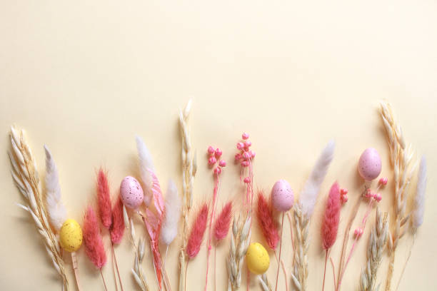 Colorful Easter eggs and pastel dried spring flowers on beige background with copy space