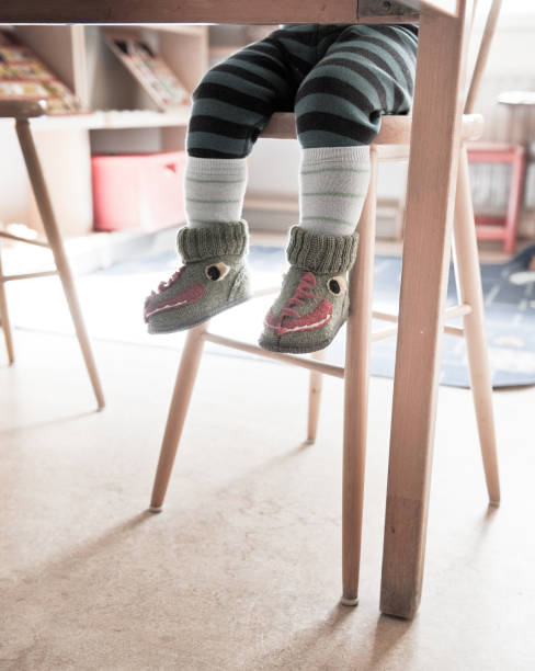 istock Kid with monster textile shoes sitting on a tall chair. 2202560149