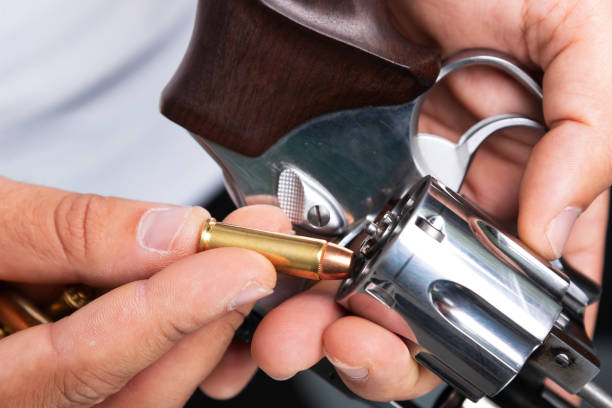 istock Detail of a shooting instructor loading a bullet into a silver revolver. Isolated on a gray background. Sports practice. 2202560899