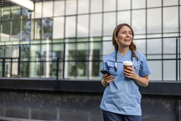 istock Smiling doctor drinking coffee and using smartphone outside hospital 2202568626