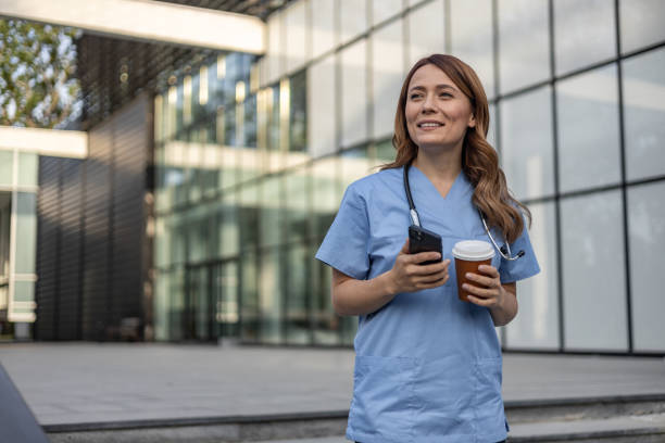 istock Smiling doctor drinking coffee and using smartphone outside hospital 2202568645