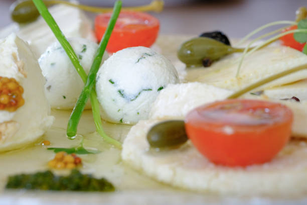 Close-up of an appetizer featuring various types of cheese, arranged artfully with cherry tomatoes, capers, and fresh herbs.  A light, flavorful presentation.