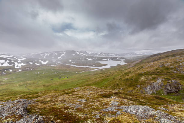 Breathtaking Norwegian Landscape Under Dramatic Skies Featuring Snow-Capped Mountains and Evocative Green Valleys Captured in a Misty Atmosphere Perfect for Nature Enthusiasts