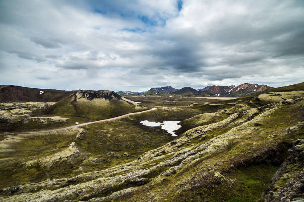 istock Breathtaking Icelandic Landscape: Rolling Hills and Snow-Capped Mountains Under a Dramatic Sky with Clouds and a Scenic Road in the Distance 2202580339