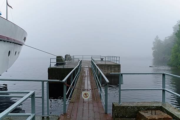 Valaam Island, Russia, July 12, 2024.  View of a large lake on a foggy summer day, concrete pier for boats on the lake, wooden decking and fences, forest in fog, bow of a moored motor ship, river transport, picturesque view, lake landscape, water surface, rivers and lakes, recreation and travel, summer.