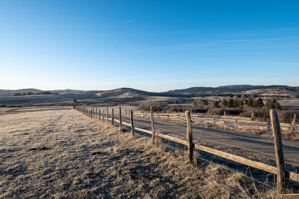 istock A frosty morning reveals a rural landscape a road winding through fields bordered by a rustic wooden fence 2202589234