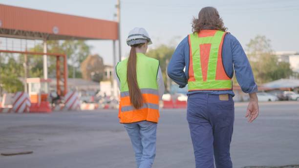 istock Rear view. Male manager talking with female engineer or supervisor about container maintenance system and tools and facilities within the port to load and unload goods cargo and container from cargo freight ship for transportation in loading yard. 2202591814