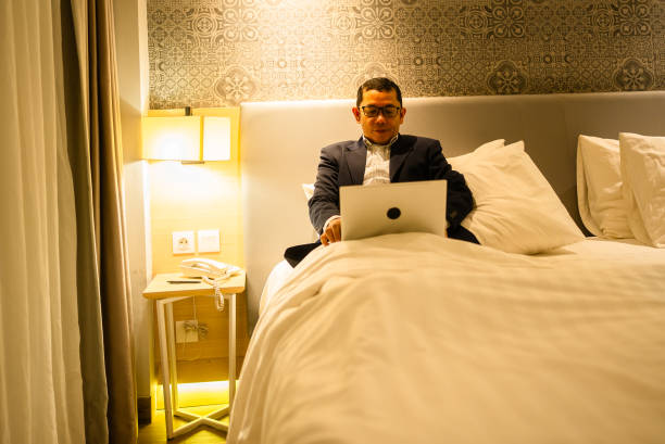 istock Businessman using laptop on bed in hotel room 2202592461