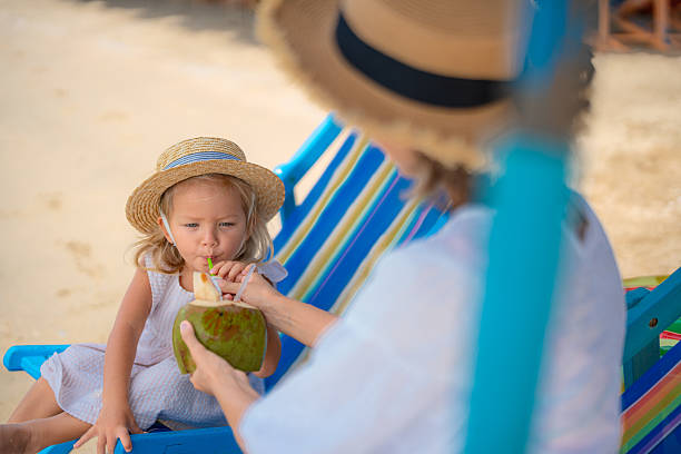 istock Young girl enjoys coconut drink while relaxing on beach chair in tropical setting 2202604143