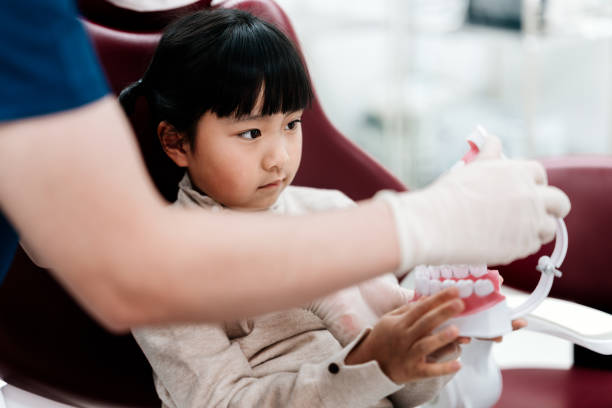 istock Dentist explaining dentistry knowledge for Asian girl, she holding teeth props while sitting at dentists chair. 2202606791