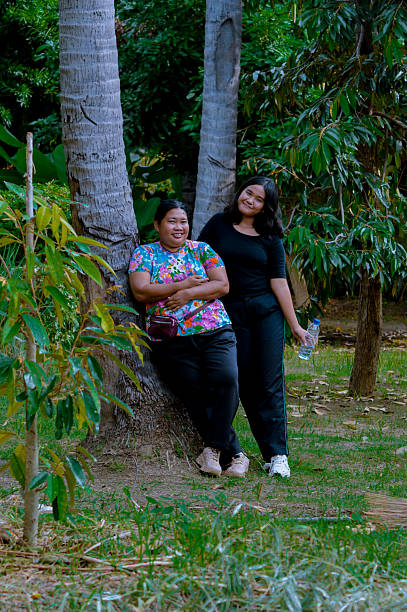 istock Two Women Relaxing Against Trees in a Lush Garden 2202607263