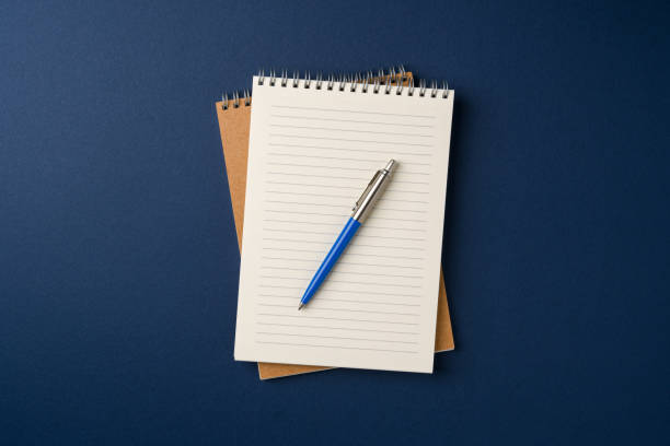 istock Top view of notebook and ballpoint pen on blue background 2202615594