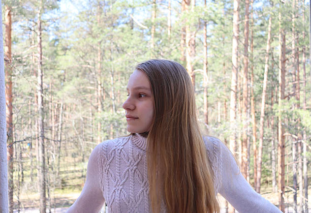 Girl with long blond hair looking somewhere. Pine forest background