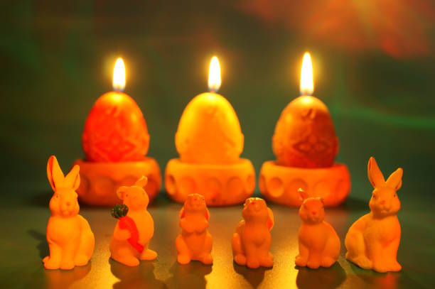 Toy rabbits and burning Easter candles on a green background.