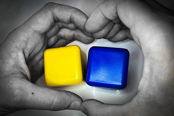 A black and white background with a hand making a heart shape around a yellow and blue cubes