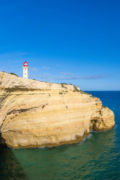 The quadrangular, white tower of the Alfanzina lighthouse stands out on a rocky promontory in the Algarve