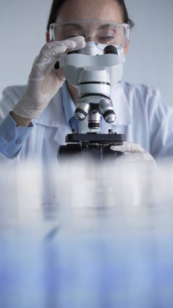 istock Woman scientist wearing white gloves, protective glasses and medical mask is using microscope doing research in modern laboratory setup. Low key lighting photo. Science and Medicine concepts 2202632879