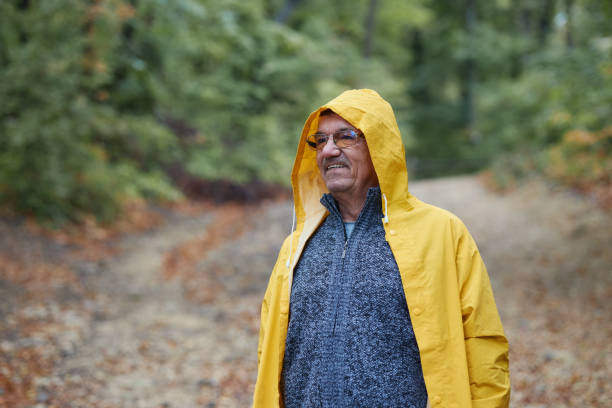 Cheerful senior man taking a walk on a rainy day at forest.