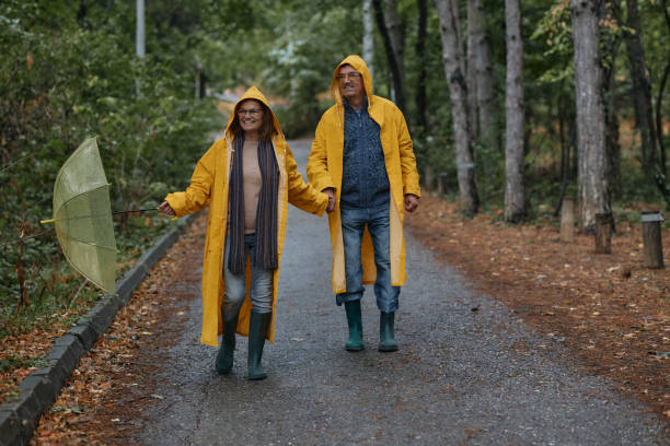 Cheerful senior embraced couple taking a walk on a rainy day at forest.