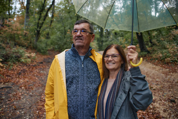 istock Happy embraced senior couple walking with umbrella at forest 2202635485