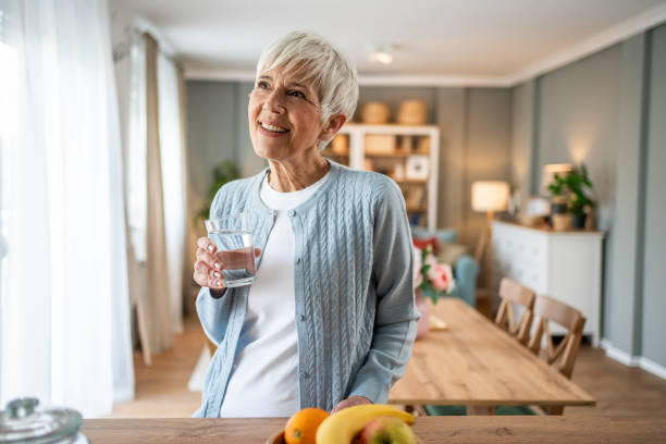 istock Senior woman drinking water and looking out the window in her kitchen 2202635596