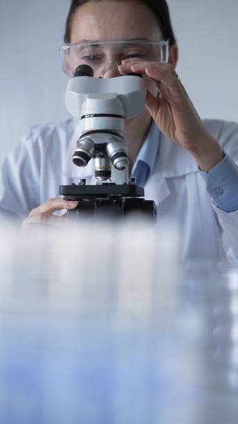 istock Woman scientist wearing lab coat and protective glasses is using microscope in modern laboratory setup. Low key lighting photo. Science and Medicine concepts 2202638663