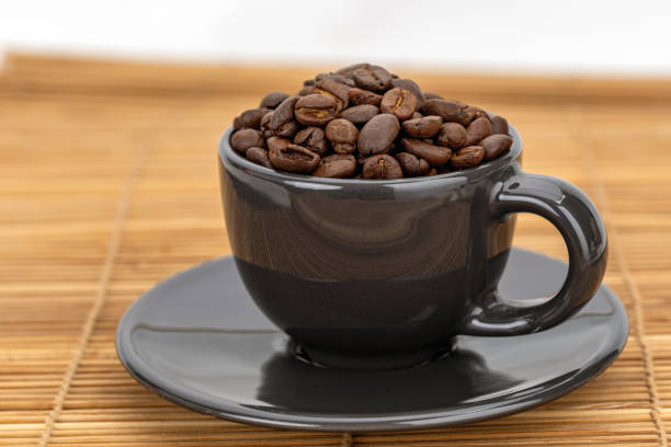 A black ceramic mug filled with roasted coffee beans gives off a rich aroma.