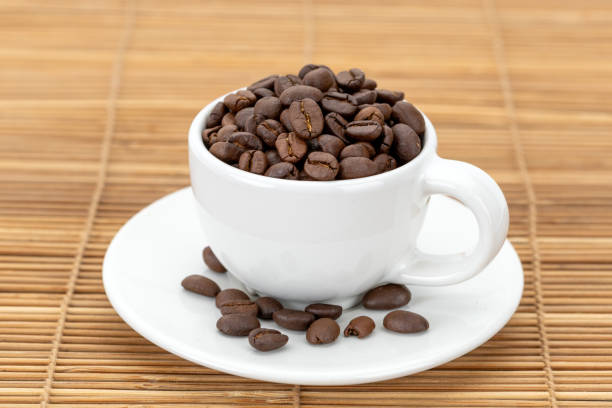 A white ceramic mug filled with roasted coffee beans gives off a rich aroma.