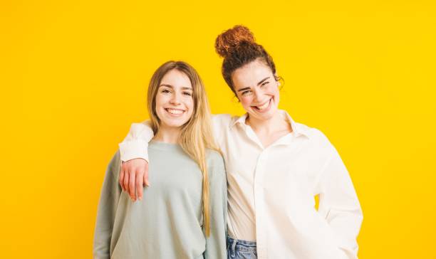 istock Two young women embracing and smiling on yellow background 2202647998