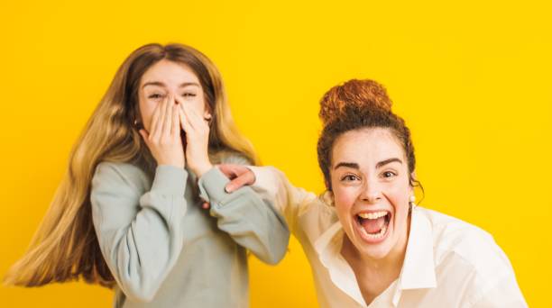 istock Two young women laughing and having fun on yellow background 2202648061