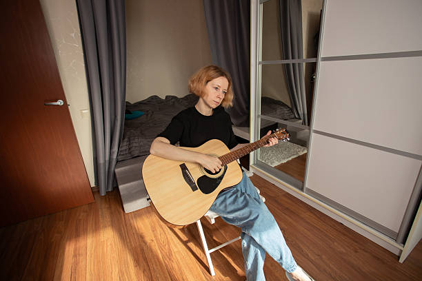 istock Woman Practicing Acoustic Guitar in Cozy Bedroom, developing guitar skills through study, learning techniques and engaging in rock melodies. 2202649984