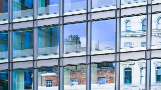 istock Towering blue glass skyscraper reflecting sky and city buildings below. 2202654275