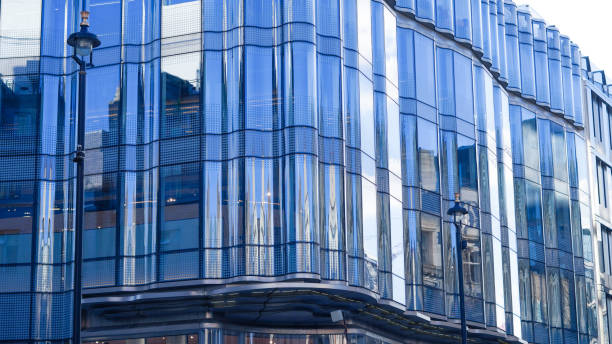 istock Towering blue glass skyscraper reflecting sky and city buildings below. 2202654454