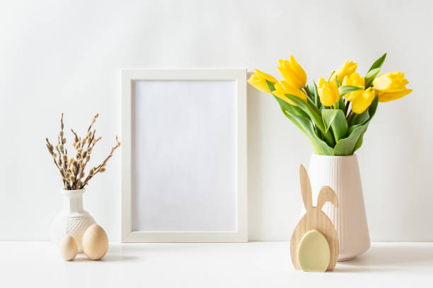 istock Mockup of a white frame with yellow tulips and eggs on a white table 2202657661
