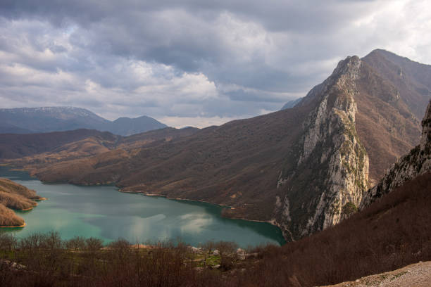 A moody landscape of a mountain range with jagged peaks towering above a deep valley. Dark clouds hover overhead, adding a dramatic and foreboding atmosphere.