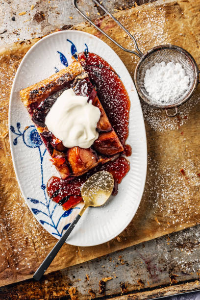 Overhead view of a dish of spiced plum and marzipan tart. Served with creme fraiche, powered sugar mixed with edible gold colored powder.