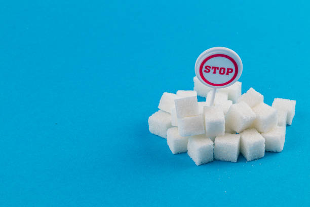 A small mound of sugar cubes is arranged on a bright blue surface, topped with a circular stop sign. This visually represents the concept of limiting sugar consumption.