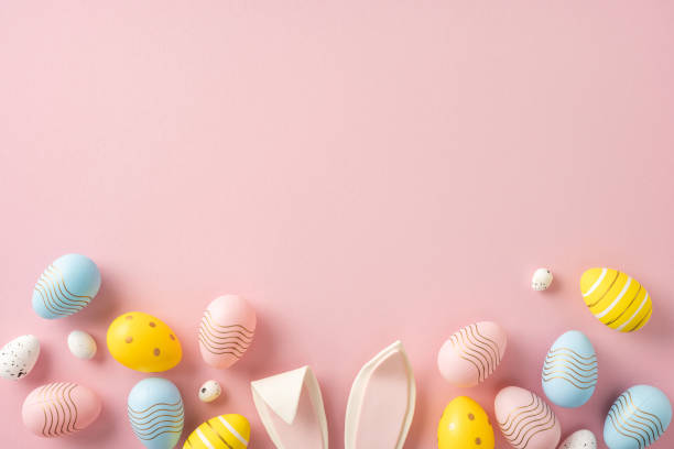istock Decorative pastel Easter eggs and bunny ears arranged on a pink surface in a festive layout 2202668698