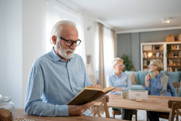 istock Senior man reading a book while two senior women chat in the background 2202675263